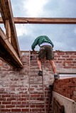 Ouvrier du bâtiment monté sur une échelle et étalant du ciment sur un mur de briques