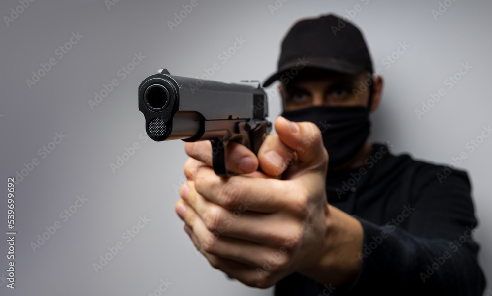 Unrecognisable male person in the black mask and pistol, outlaw and crime concept Unrecognisable male person in the black mask and pistol, outlaw and crime concept