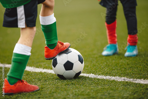Legs of Soccer Player Kicking Classic Soccer Ball. School Kids Practicing Football Skills at Training Pitch © matimix