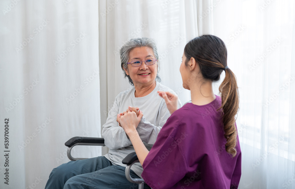 Asian young nurse taking care and talking mature female patient sitting on wheelchair in hospital. Healthcare concept. Asian young nurse taking care and talking mature female patient sitting on wheelchair in hospital. Healthcare concept.