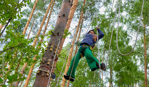 Child wins by climbing high rope, wearing mountain helmet and protective gear. Rope adventure park. The concept of sport, healthy lifestyle, strength, training.