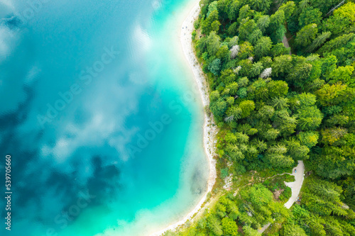 Aerial view of a lake with turquoise water and clouds reflection and pine trees on the shore. 