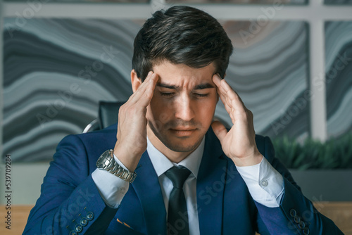 Stress and anxiety. Tired thinking businessman working with laptop in modern office. General manager,ceo. Young handsome confident man in suit sitting at table,workplace. Executive business career