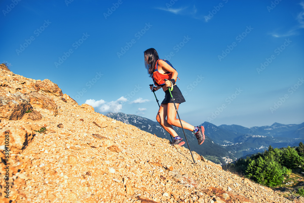 Woman climbs a rocky slope with poles