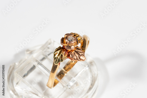 multicolored gold diamond ring on a white background, flower and grape leaves in a frame