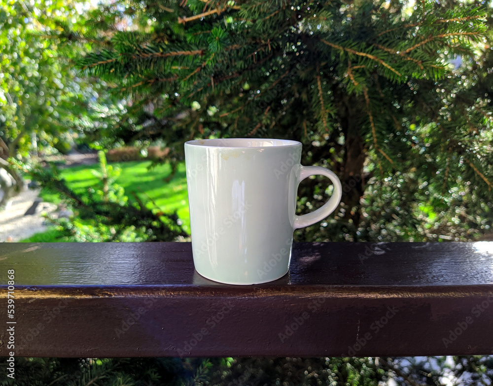 white cup along with coffee on the railing of the house and garden background. white cup along with coffee on the railing of the house and garden background.
