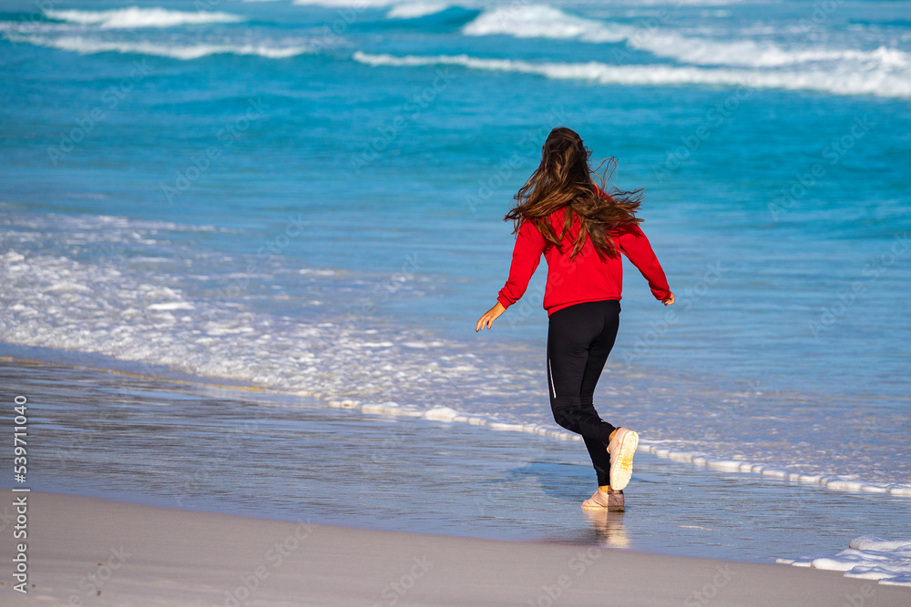 Back view of a long-haired girl running along the ocean shore on a paradise beach at sunset; turquoise water on a beach in lucky bay, western australia, running on the beach Back view of a long-haired girl running along the ocean shore on a paradise beach at sunset; turquoise water on a beach in lucky bay, western australia, running on the beach