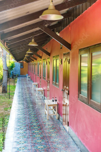 Long open empty terrace with red wall, tile floor and row of windows and wooden doors in asian hotel