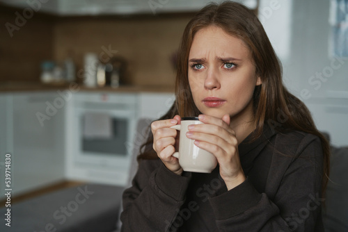 Fototapeta Naklejka Na Ścianę i Meble -  Caucasian sad woman sitting at the sofa with cup of coffee