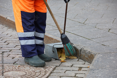 Worker in uniform with a broom clean the sidewalk, collects fallen leaves in a dustpan. Street cleaning in autumn city