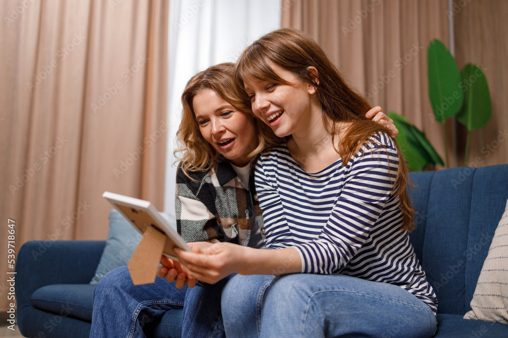 Young woman is having fun with her mother looking through old childhood photos Young woman is having fun with her mother looking through old childhood photos