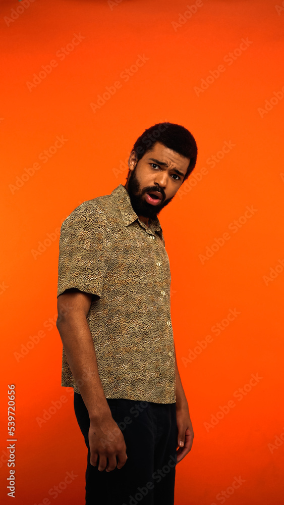 vertical view of shocked african american man with beard and opened mouth on orange. vertical view of shocked african american man with beard and opened mouth on orange.