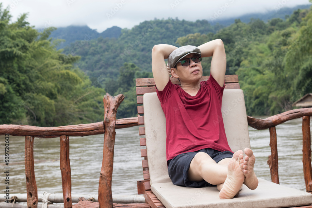 The man relaxed man in a crimson t-shirt enjoying nature breathing fresh air meditating on the river on a vacation day.

