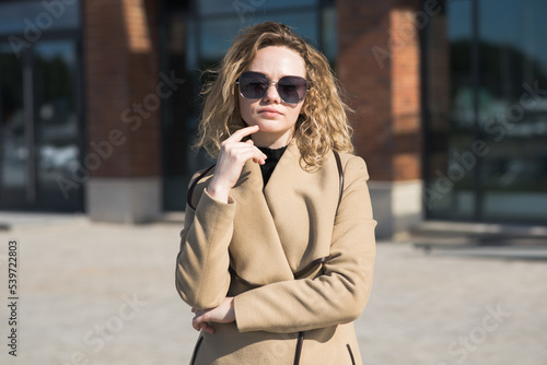 Portrait of a young Caucasian girl in a coat and sunglasses in the city on an autumn day.