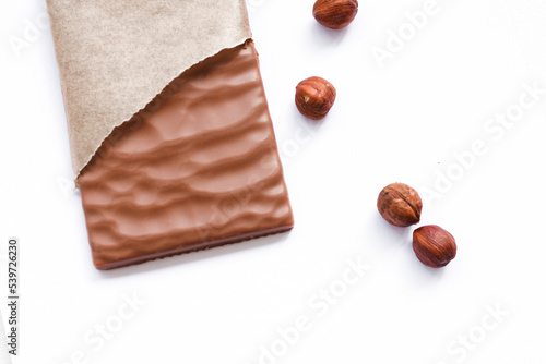 Chocolate bar with hazelnuts in opened pack on white table background. Closeup