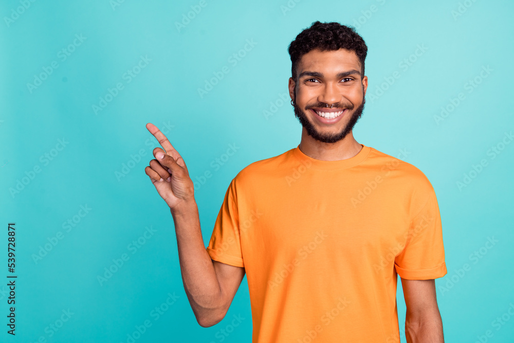 Photo of sweet good mood man dressed orange t-shirt pointing finger empty space isolated turquoise color background Photo of sweet good mood man dressed orange t-shirt pointing finger empty space isolated turquoise color background