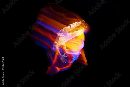 In miracle flight. Young sportive dancer in white clothes levitating, moving over dark background in mixed neon light. Creative art, aspiration, music, fashion, dance photo