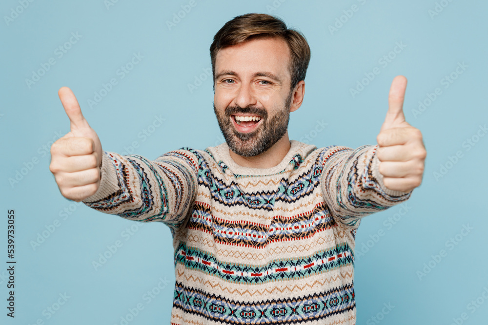 Young smiling happy satisfied cheerful caucasian man 30s he wear sweater showing thumb up like gesture isolated on plain pastel light blue cyan background studio portrait. People lifestyle concept. Young smiling happy satisfied cheerful caucasian man 30s he wear sweater showing thumb up like gesture isolated on plain pastel light blue cyan background studio portrait. People lifestyle concept.