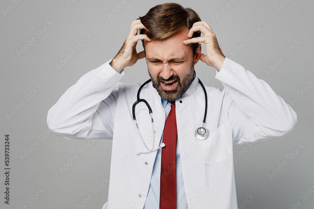 Sideways stressed male doctor man wearing white medical gown suit stethoscope work in hospital scratch hold head isolated on plain grey color background studio portrait. Healthcare medicine concept. Sideways stressed male doctor man wearing white medical gown suit stethoscope work in hospital scratch hold head isolated on plain grey color background studio portrait. Healthcare medicine concept.