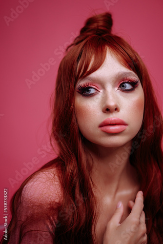  Beautiful young woman with red hair and bright pink makeup on a pink background. The gaze is directed to the side