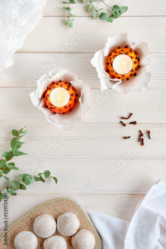 Eucalyptus twigs, natural orange tea light with cloves and gingerbread cookies, lebkuchen on ceramic board. Flat lay, top view on off white rustic wooden planks. photo