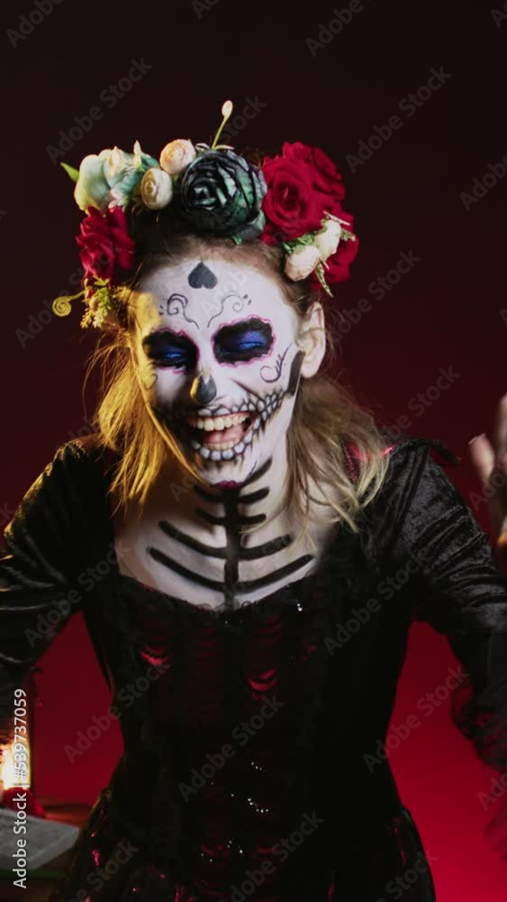 Vertical video: Horror goddess of death yelling in costume with skull body art, wearing flowers crown and screaming like holy santa muerte to celebrate dios de los muertos. Woman on tranditional Vertical video: Horror goddess of death yelling in costume with skull body art, wearing flowers crown and screaming like holy santa muerte to celebrate dios de los muertos. Woman on tranditional