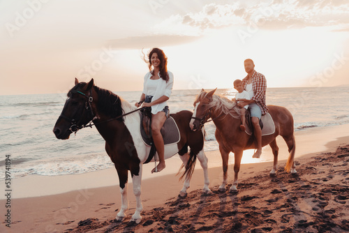 The family spends time with their children while riding horses together on a sandy beach. Selective focus  © .shock