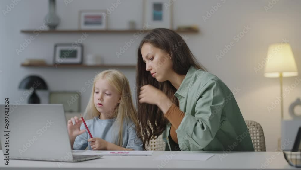 A young woman mom or babysitter helps the girl do her homework by talking and commenting . A caring mom or nanny explains the topic of lessons, coloring the drawing together A young woman mom or babysitter helps the girl do her homework by talking and commenting . A caring mom or nanny explains the topic of lessons, coloring the drawing together