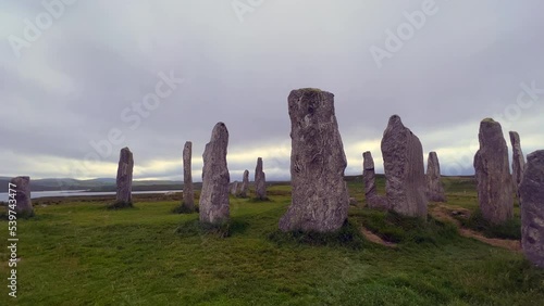 Moving around the standing stones or megaliths of the Callanish or Calanais stone circle in a cloudy evening. Sun peeking through the could, magic, ancient, neolithic atmosphere. Archaeological sites. photo