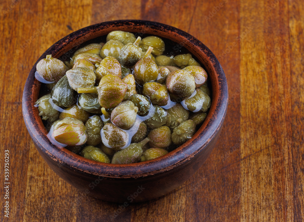 Clay bowl with capers stands on a wooden table. Clay bowl with capers stands on a wooden table.
