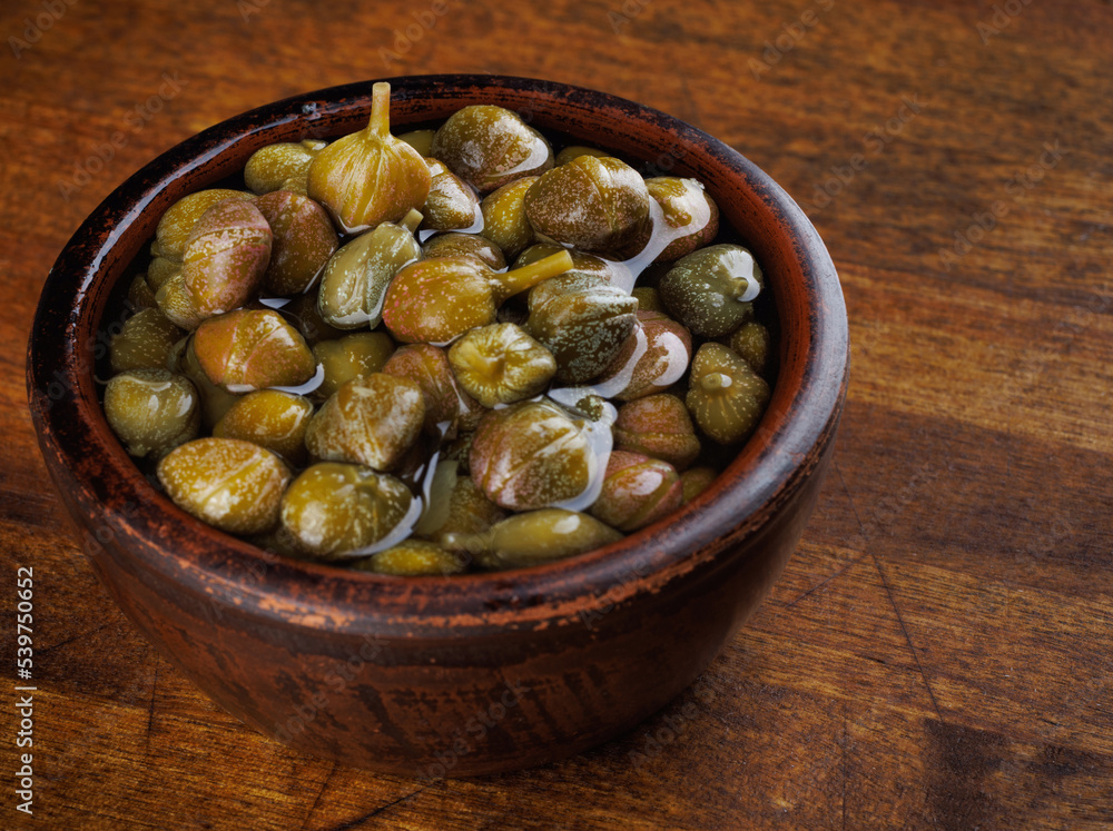 A bowl of pickled capers stands on a wooden surface. A bowl of pickled capers stands on a wooden surface.
