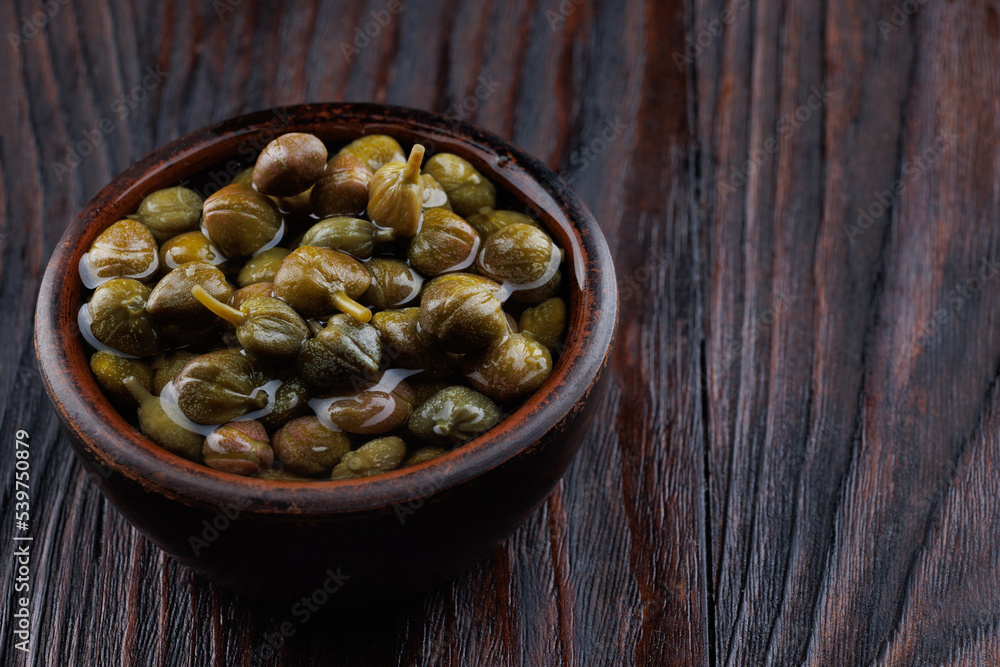 Pickled capers in a clay cup on a wooden table. Pickled capers in a clay cup on a wooden table.
