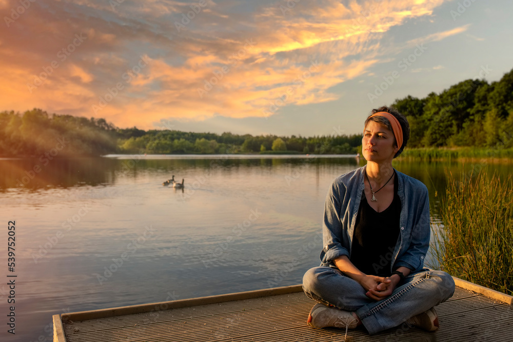 woman sitting and relaxing on the edge of a lake at sunset woman sitting and relaxing on the edge of a lake at sunset