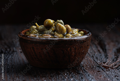 Photos Pickled capers in brine. Clay cup full of capers.