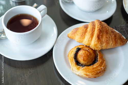 Bread  croissant in a white plate with a glass of tea on the breakfast table.