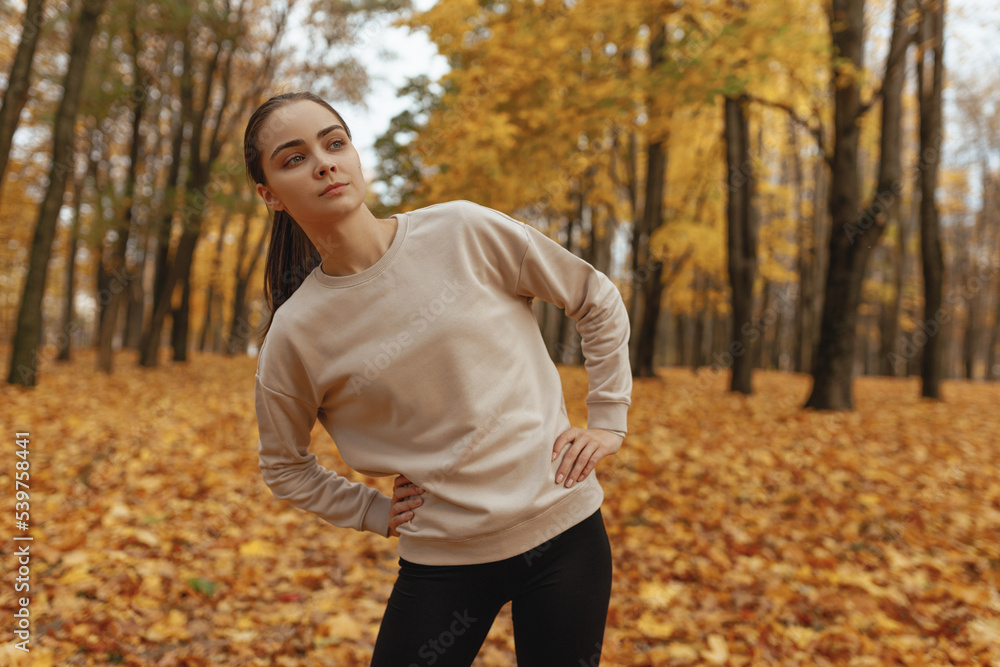 Sporty woman in activewear doing side bend exercise and stretching during training in autumn in nature Sporty woman in activewear doing side bend exercise and stretching during training in autumn in nature