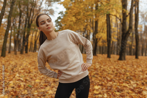 Sporty woman in activewear doing side bend exercise and stretching during training in autumn in nature 
