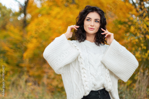 Beautiful woman in a fashionable knitted white sweater walks and poses in a bright autumn yellow park with colorful fall foliage