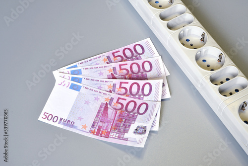 Euro banknotes and electrical extension socket on a gray background. Concept for the rising cost of electricity. Expensive energy bill and rising electricity prices.