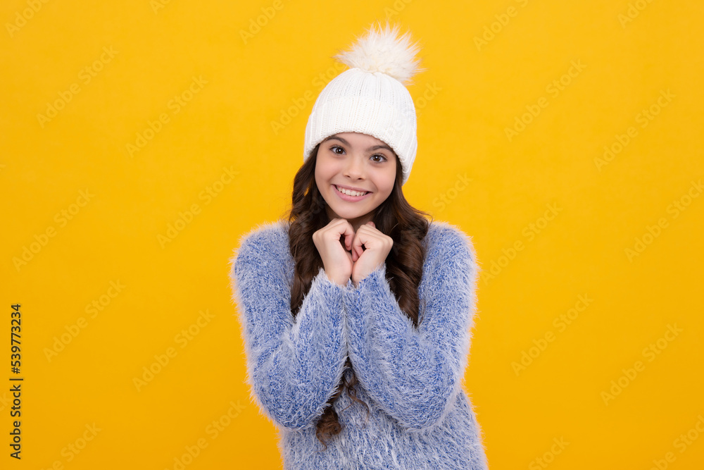 Beautiful teen girl in a winter hat and a warm sweater. A child on a yellow isolated background. Happy girl face, positive and smiling emotions. Beautiful teen girl in a winter hat and a warm sweater. A child on a yellow isolated background. Happy girl face, positive and smiling emotions.