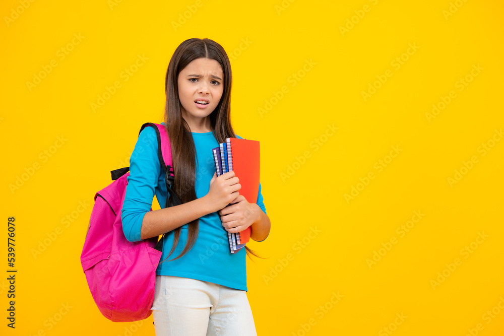 Back to school. Teenager schoolgirl hold book and copybook ready to learn. School children on isolated yellow studio background. Angry face, upset emotions of teenager girl. Back to school. Teenager schoolgirl hold book and copybook ready to learn. School children on isolated yellow studio background. Angry face, upset emotions of teenager girl.