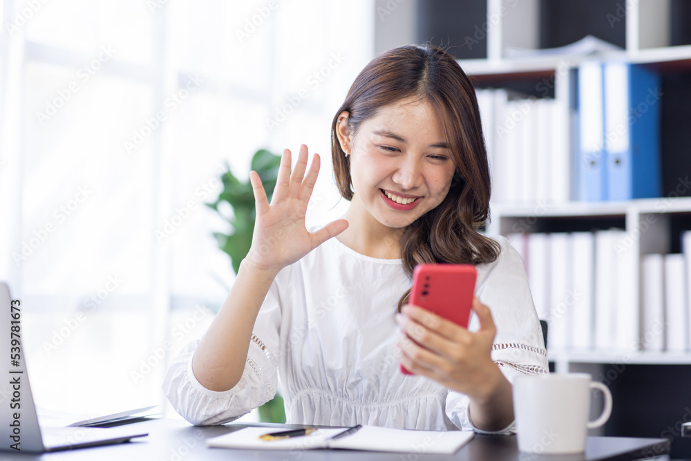 Young Business Asian woman using phone and works on laptop computer in the modern home office. Young Business Asian woman using phone and works on laptop computer in the modern home office.