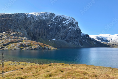 view on a lake borded by snow-capped mountain and yellow grass in Norway
