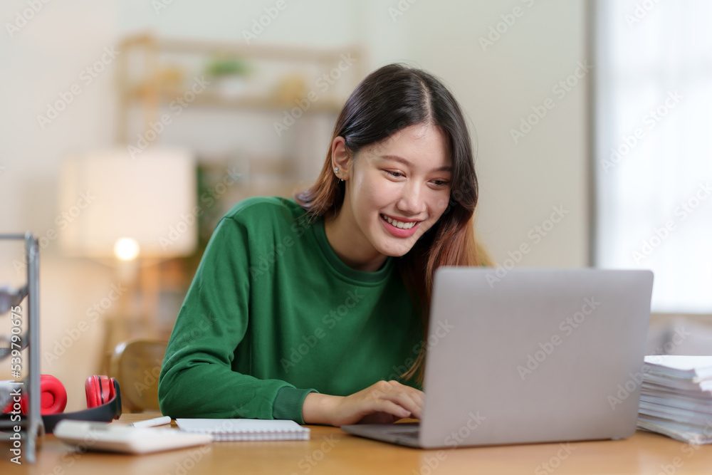 Beautiful young Asian female college students smiling happily using their laptop computer to study online at home comfortably. Asian woman using laptop at home Beautiful young Asian female college students smiling happily using their laptop computer to study online at home comfortably. Asian woman using laptop at home