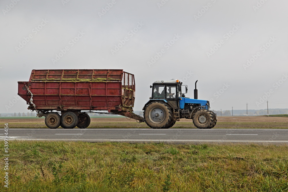 Wheeled tractor transportate a heavy trailer on countryside highway road