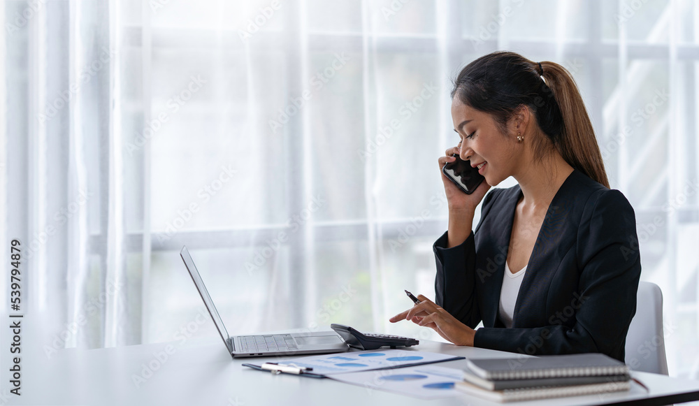 Attractive Asian businesswoman Use your laptop to watch your computer and talk on phone. Consult customers, sit at a table. financial officer making a mobile business call Discuss work with clients Attractive Asian businesswoman Use your laptop to watch your computer and talk on phone. Consult customers, sit at a table. financial officer making a mobile business call Discuss work with clients