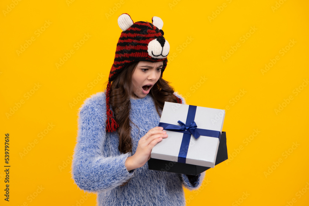Child with gift present box on isolated yellow background. Presents for birthday, Valentines day, New Year or Christmas. Shocked amazed face, surprised emotions of young teenager girl.