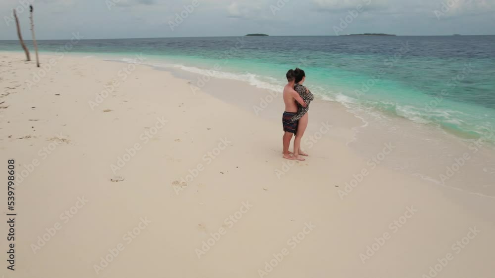 Aerial circular pan shot of young couple hug on the beach in Maldives, turquoise waves splashing. Concept of romantic trip and honeymoon Aerial circular pan shot of young couple hug on the beach in Maldives, turquoise waves splashing. Concept of romantic trip and honeymoon