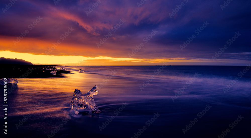 Beautiful colorful sunset over icy ocean and winter sea with iceberg chunks resting on a dramatic black sand beach in Iceland. 