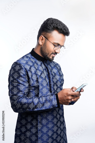 Happy handsome indian man wearing traditional outfit holding or using mobile phone celebrating diwali festival and giving expression